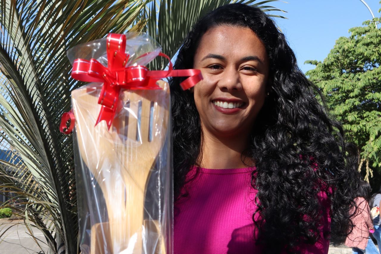 Uma mulher está segurando uma colher de pau embrulhada em plástico com um laço vermelho.