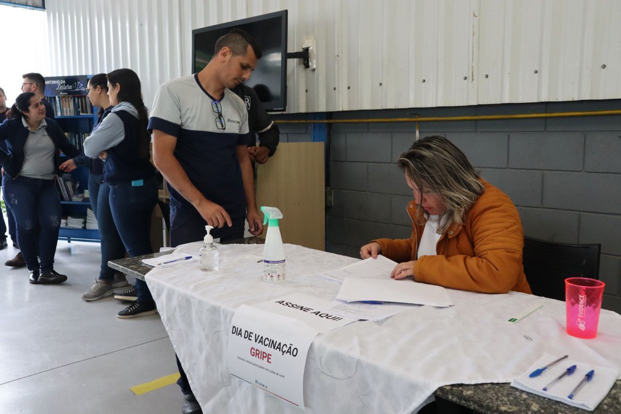 Uma mulher está sentada à mesa em frente a um grupo de pessoas.