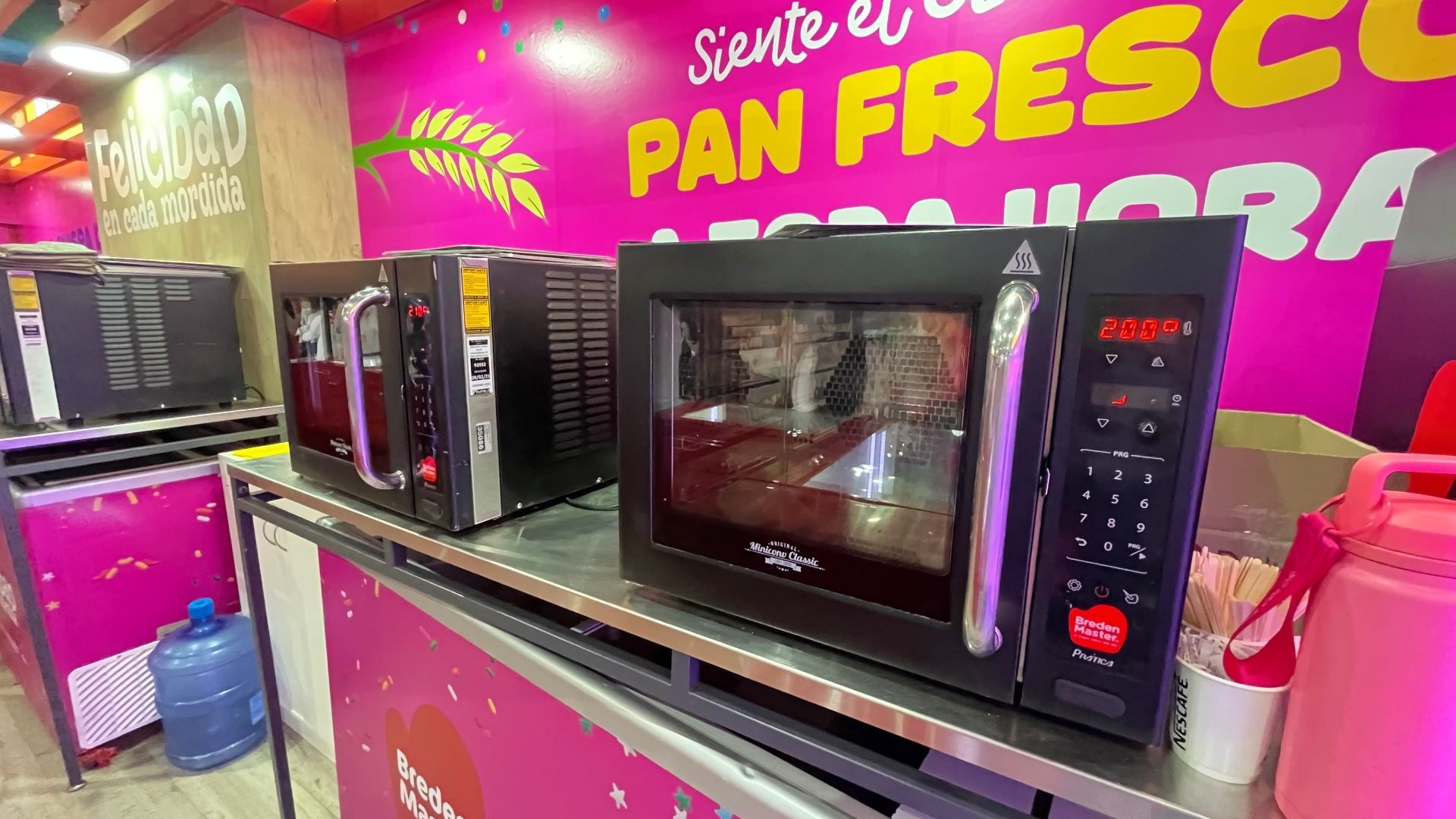 Micro-ondas em um balcão em uma padaria de cores vibrantes; o fundo tem texto rosa.