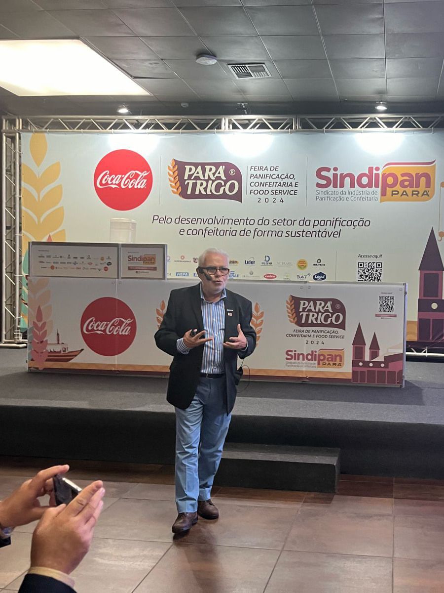Um homem está em pé no palco em frente a uma placa da Coca-Cola.