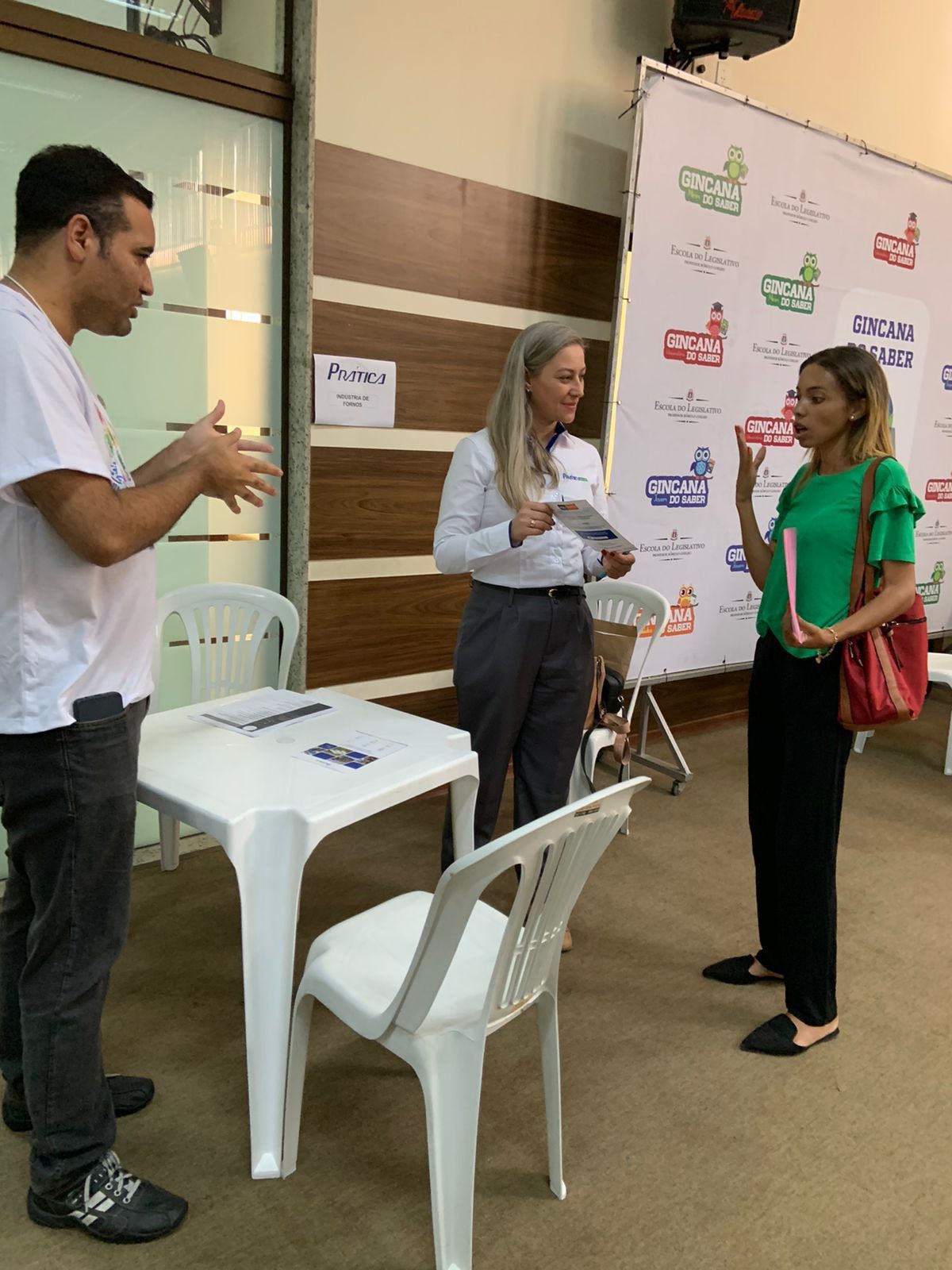 Um homem e duas mulheres estão em pé ao redor de uma mesa e cadeiras.
