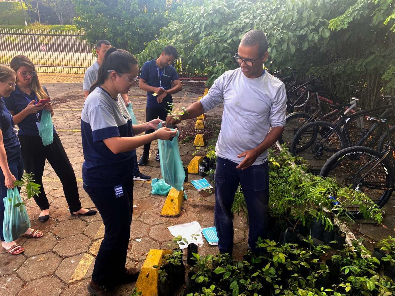Um grupo de pessoas está em pé ao redor de um monte de plantas em vasos.