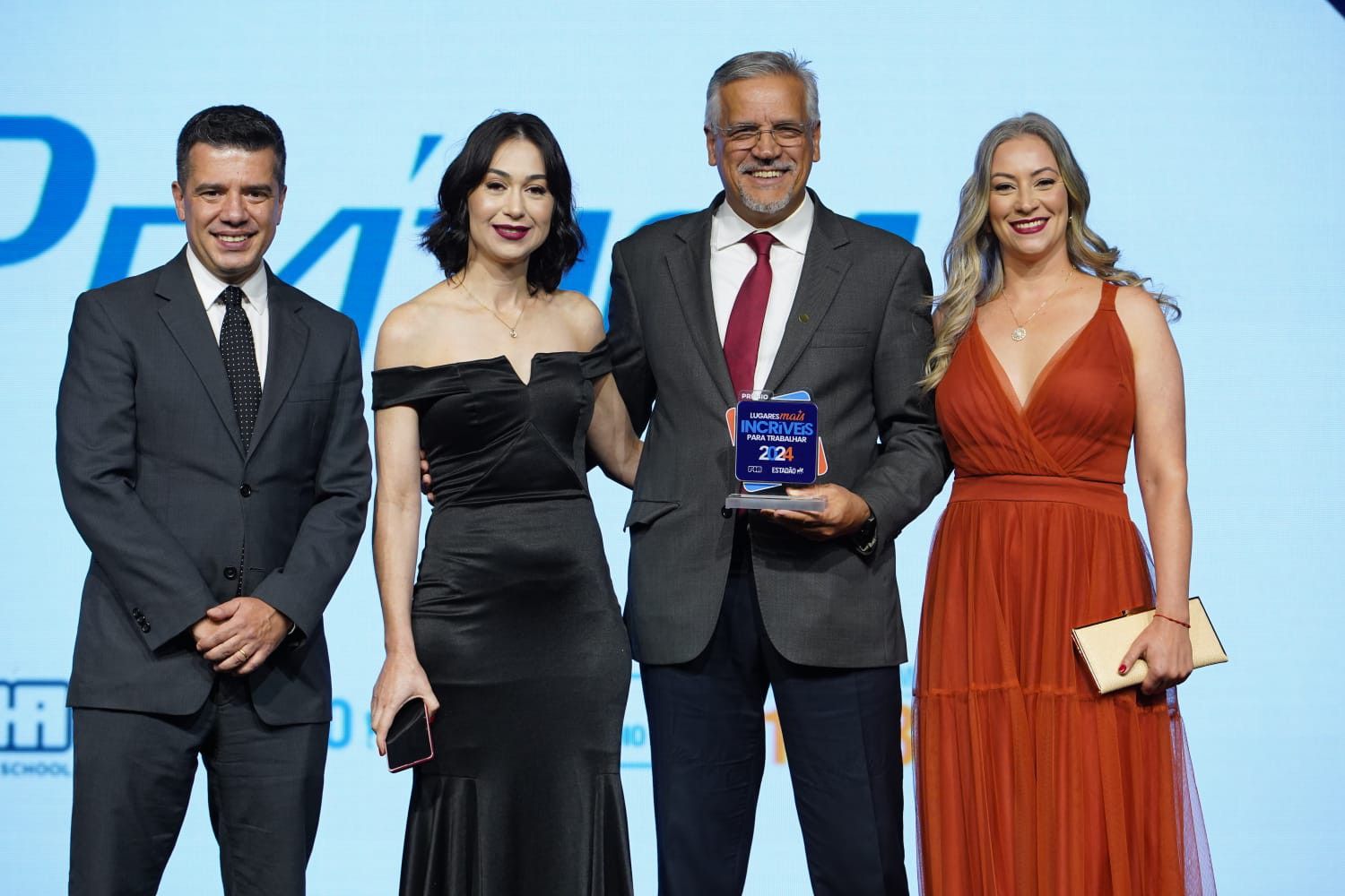 Um grupo de pessoas em pé, uma ao lado da outra, em um palco, segurando um troféu.