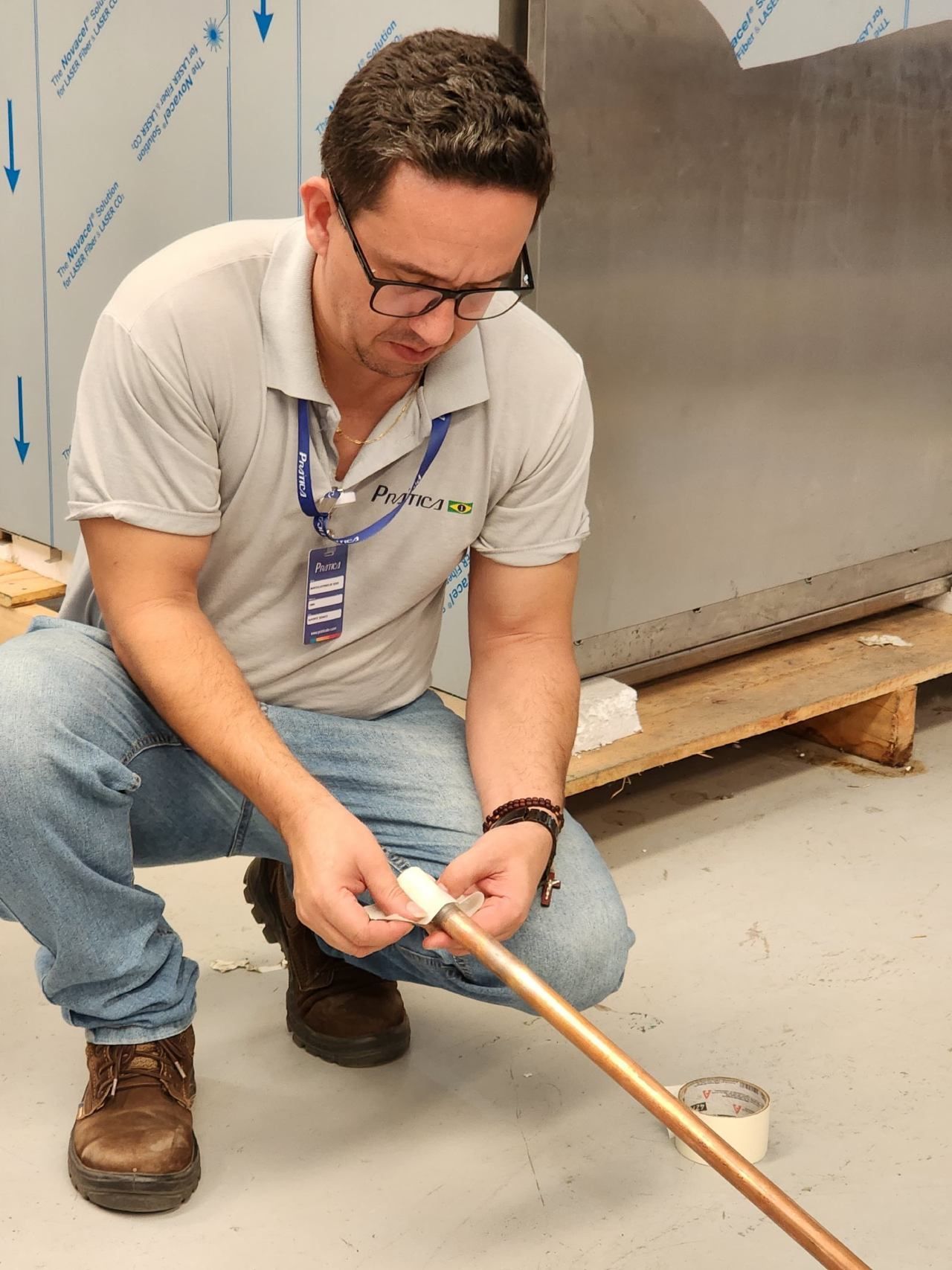 Um homem de óculos está ajoelhado e trabalhando em um cano