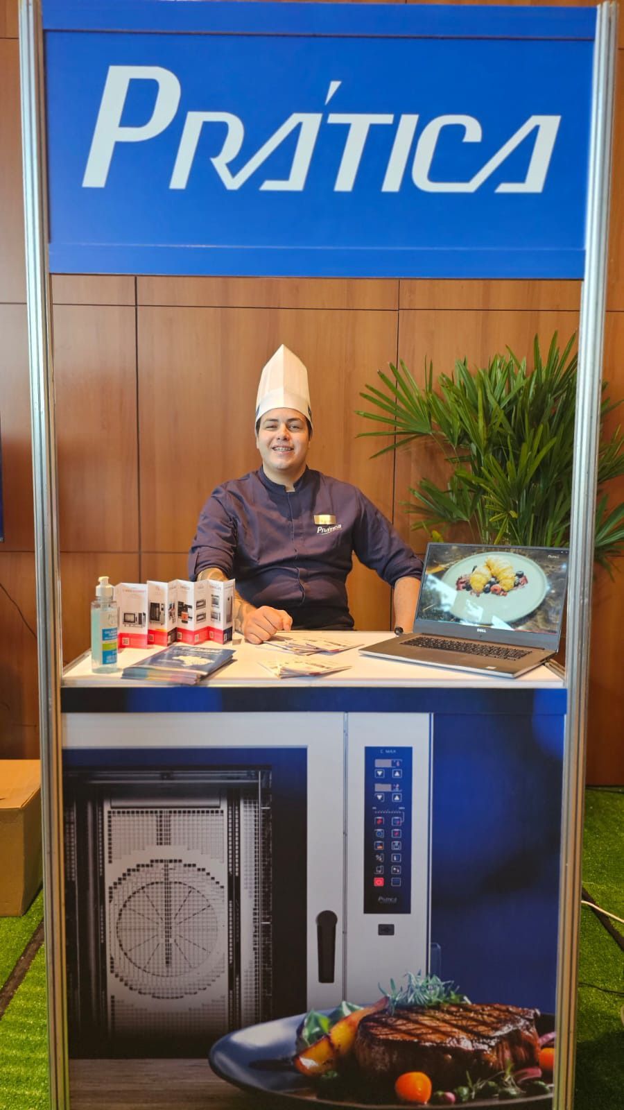 Um homem com chapéu de chef está sentado à mesa sob uma placa de prática