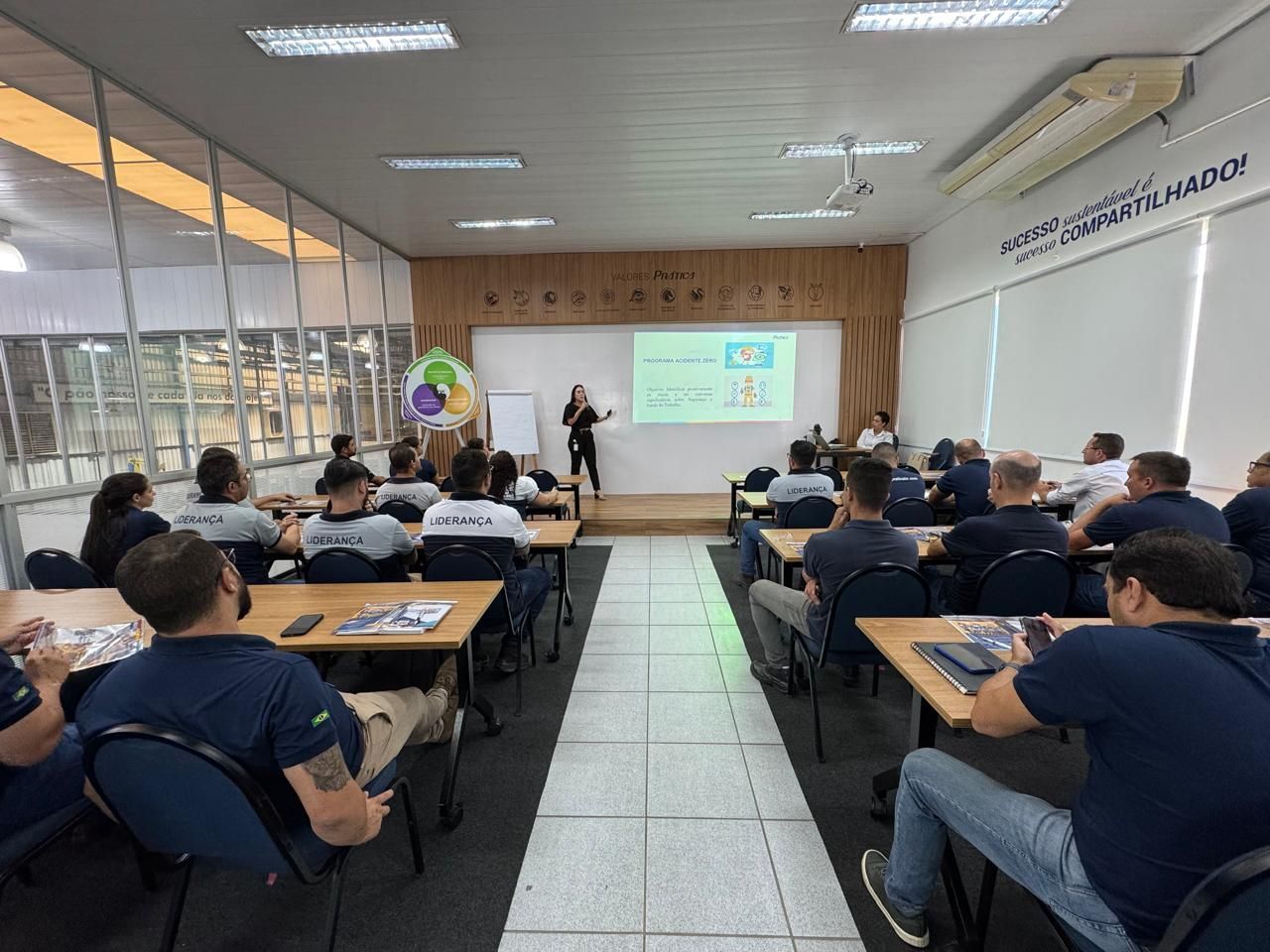Uma mulher está fazendo uma apresentação para um grupo de pessoas em uma sala de aula.
