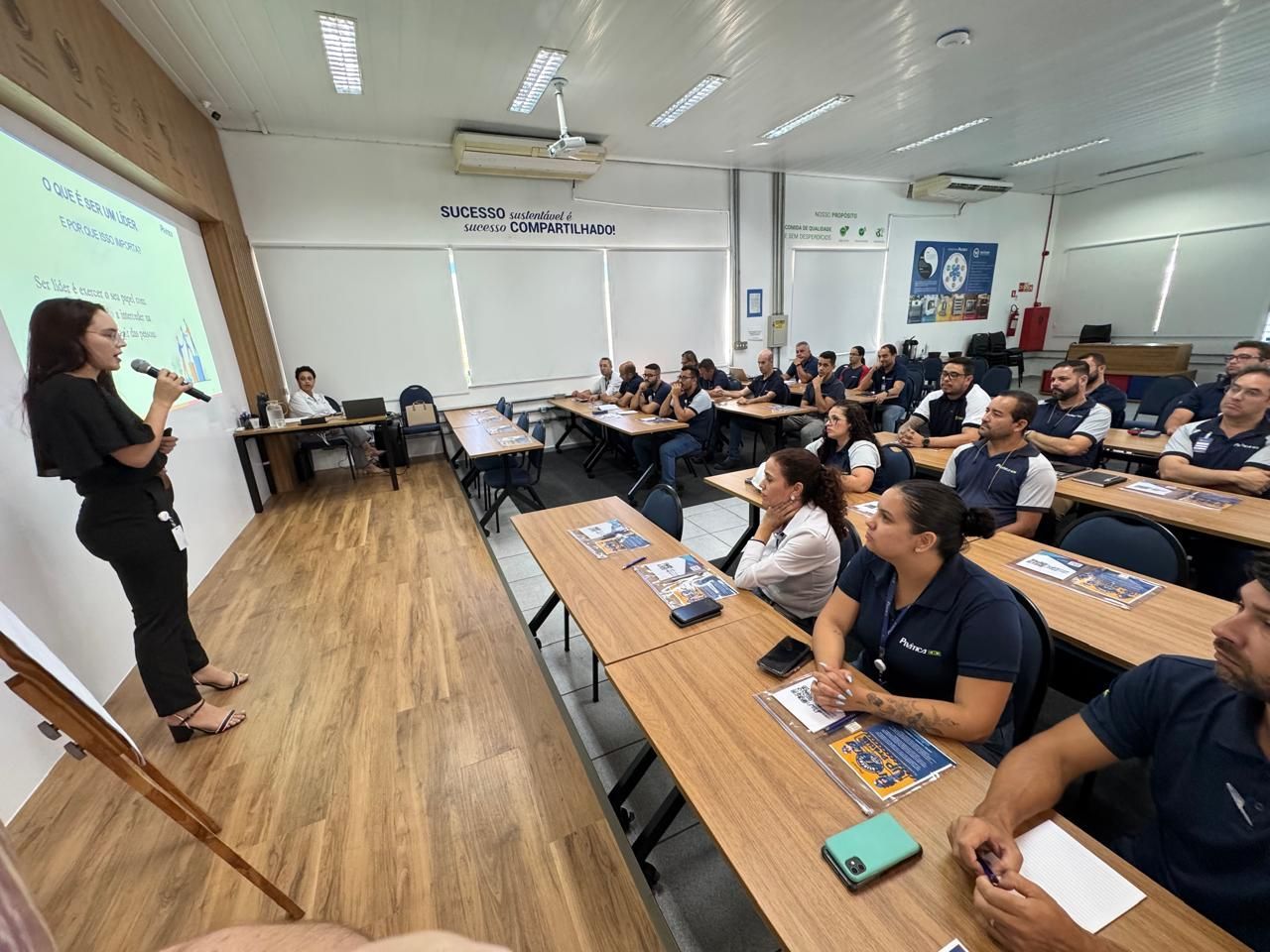 Uma mulher está fazendo uma apresentação para um grupo de pessoas em uma sala de aula.