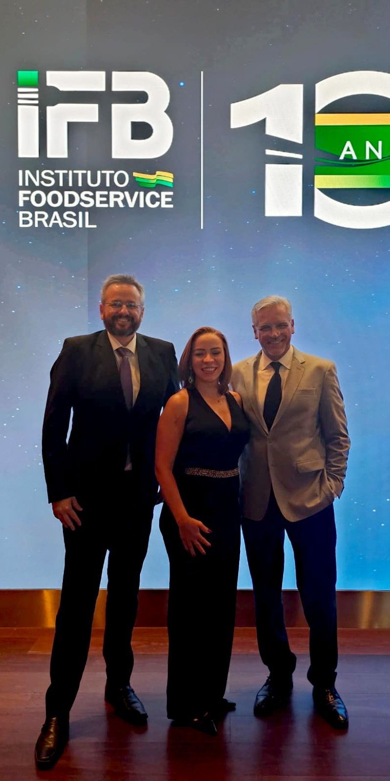 Três pessoas posam para uma foto em frente a uma placa que diz instituto foodservice brasil.