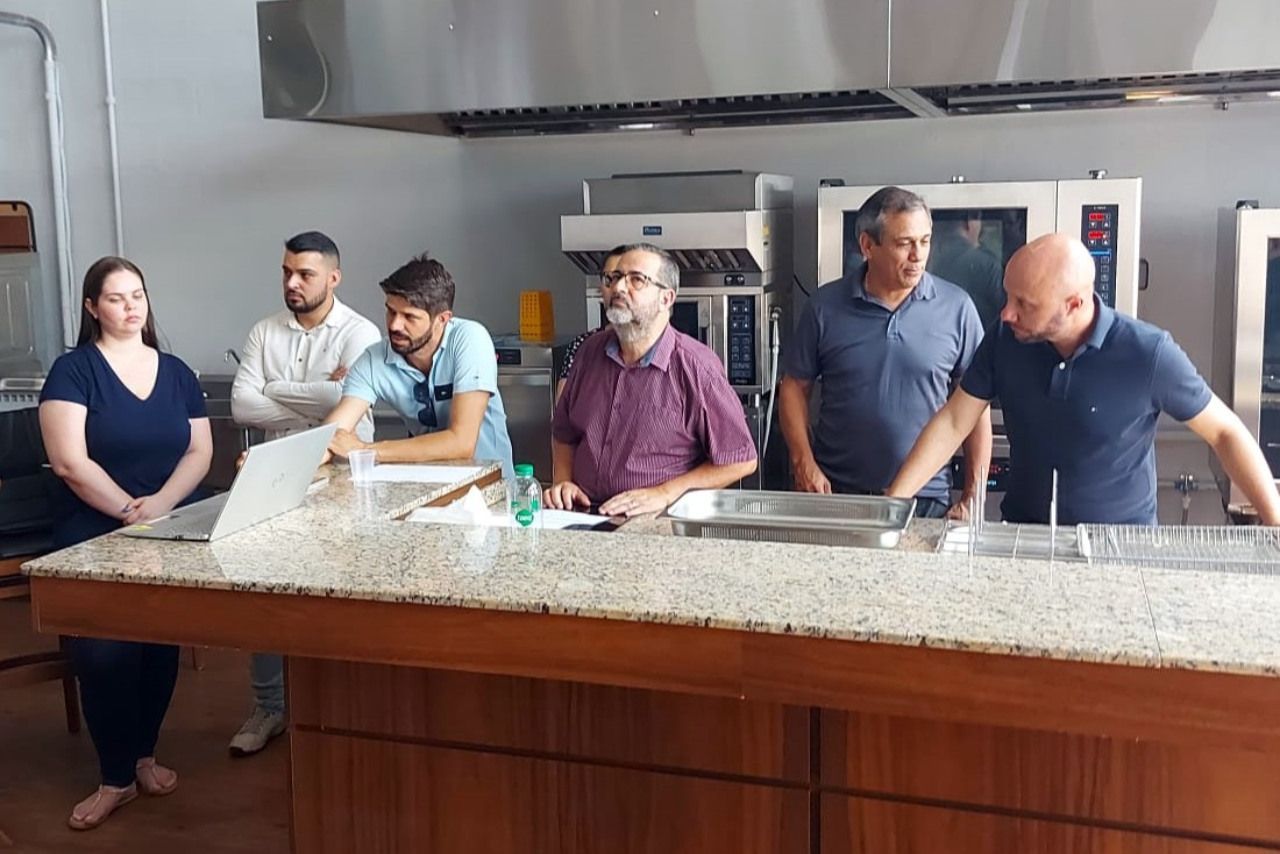 Um grupo de pessoas está em pé ao redor de um balcão na cozinha.