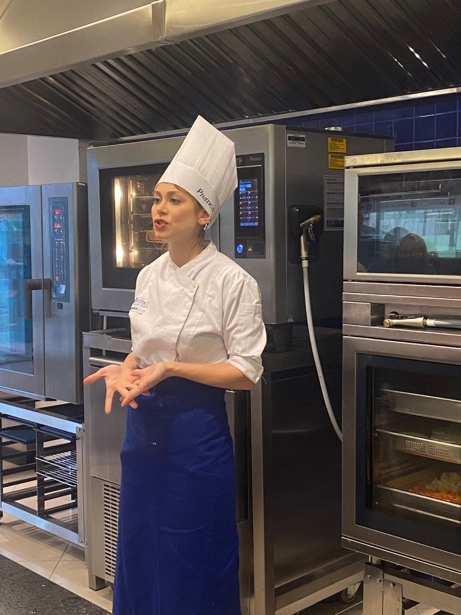 Uma mulher com um chapéu de chef está parada na cozinha.