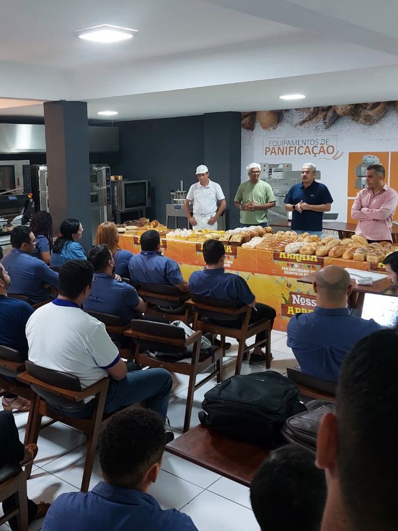 Um grupo de pessoas está sentado em cadeiras em frente a uma mesa com pão sobre ela.