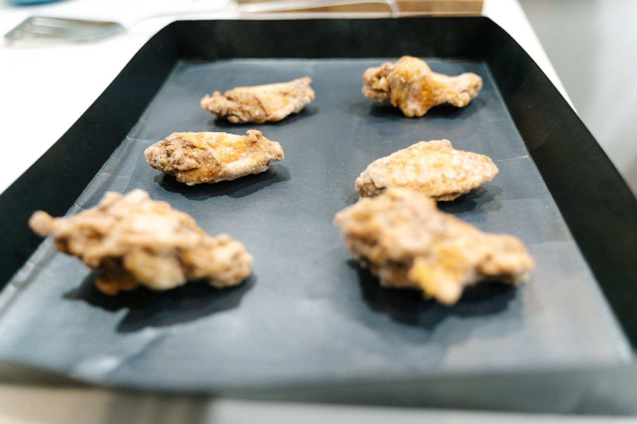 Asinhas de frango fritas estão em uma bandeja preta sobre uma mesa.