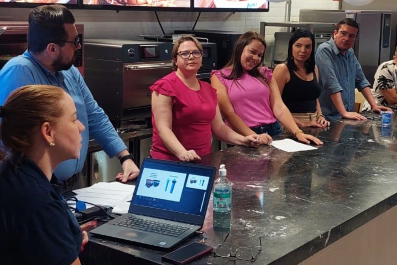 Um grupo de pessoas está sentado ao redor de uma mesa com um laptop sobre ela.
