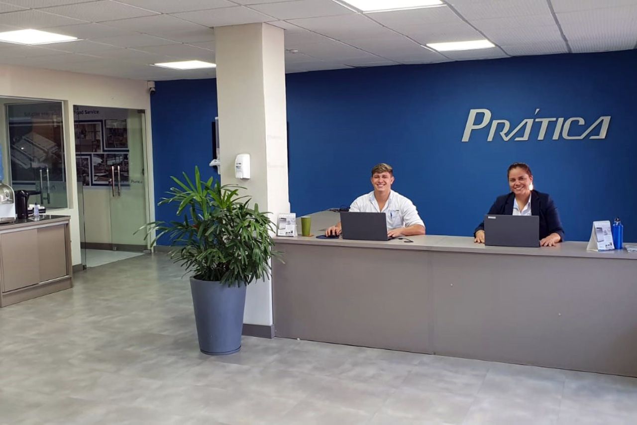 Um homem e uma mulher estão sentados em uma mesa em frente a uma placa de prática.