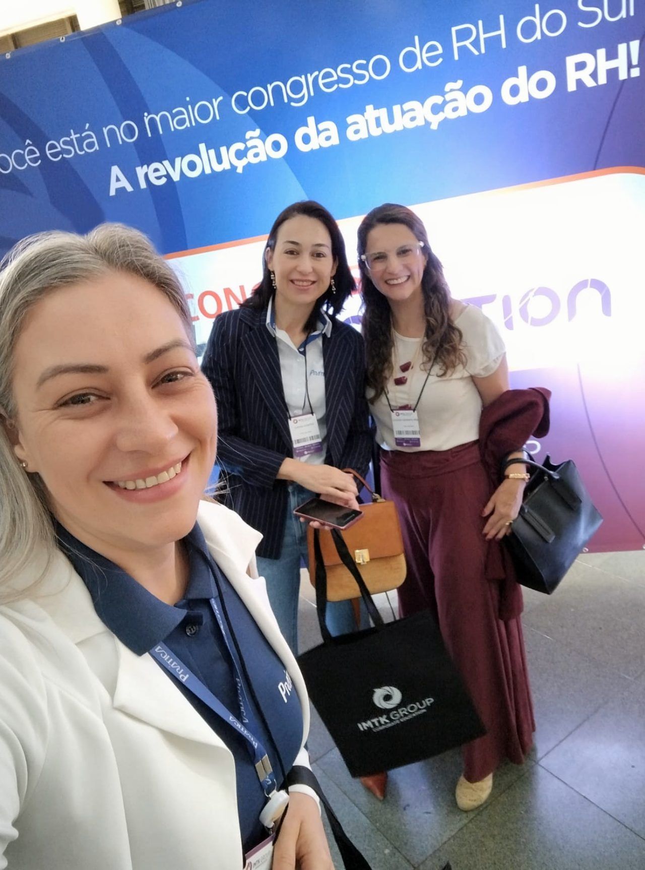 Três mulheres posam para foto em frente a uma placa que diz rh do sul