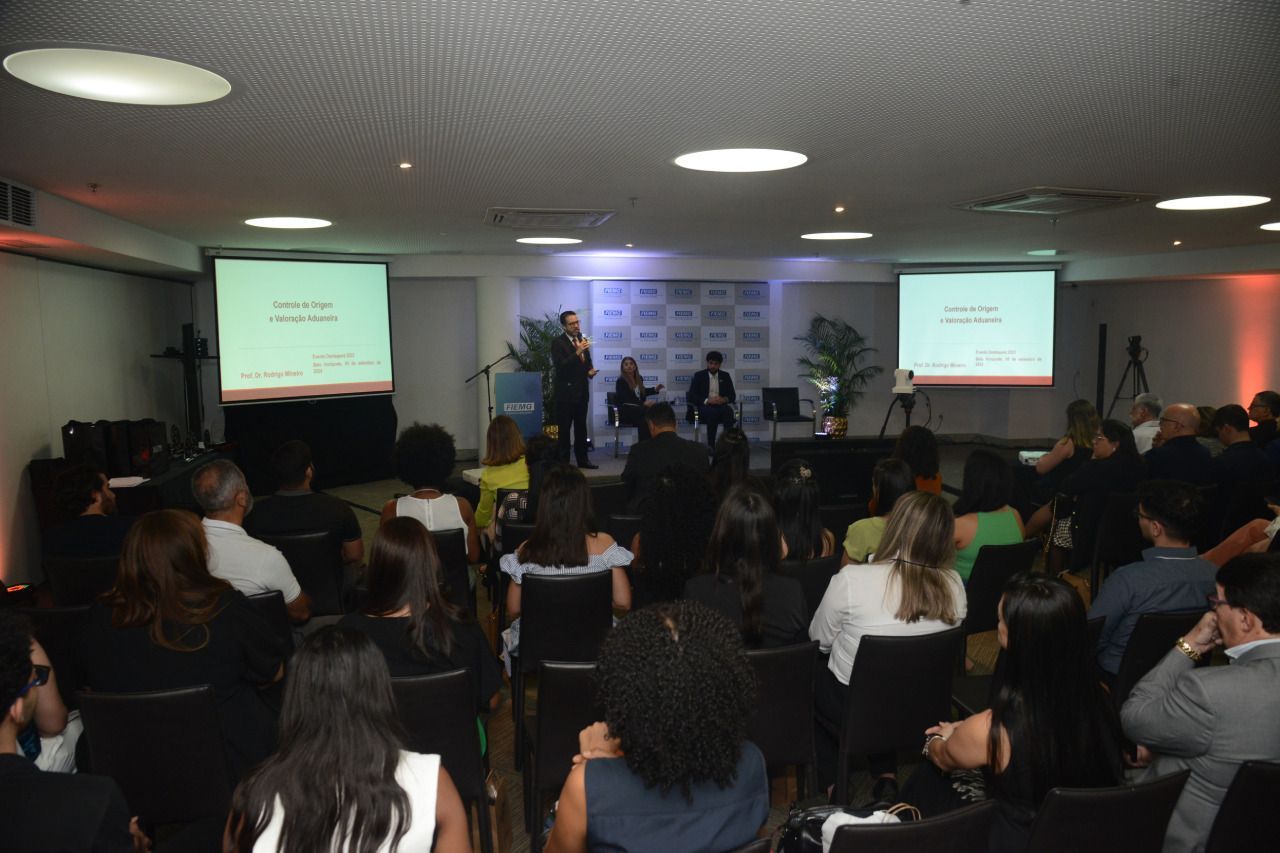 Um grande grupo de pessoas está sentado em uma sala de conferências assistindo a uma apresentação.