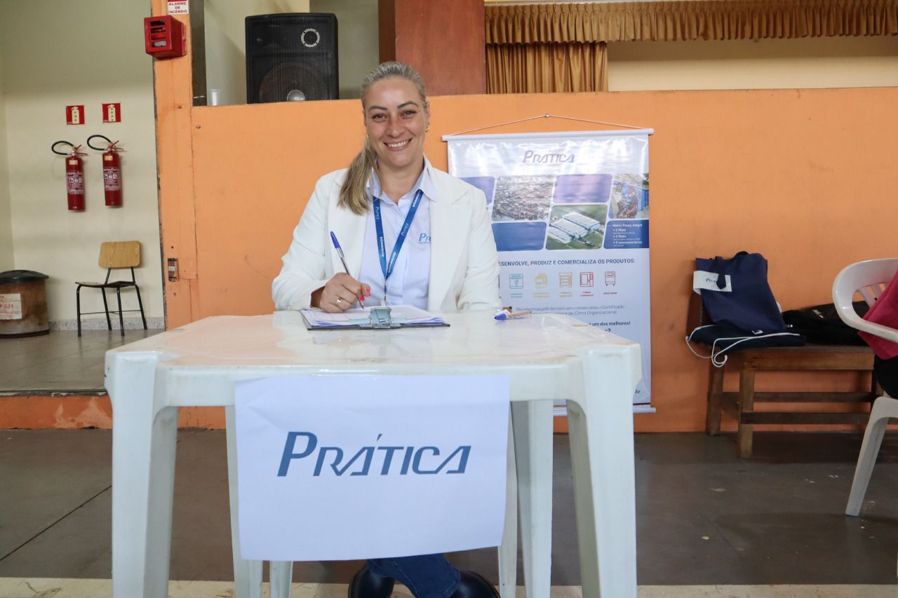 Uma mulher está sentada em uma mesa com uma placa que diz prática