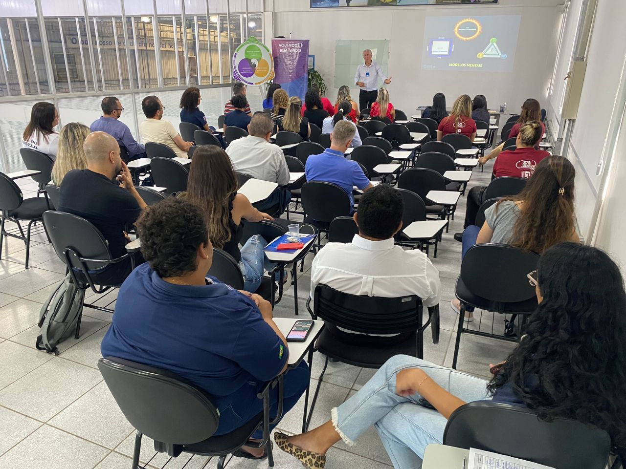 Um grupo de pessoas está sentado em uma sala de aula assistindo a uma apresentação.