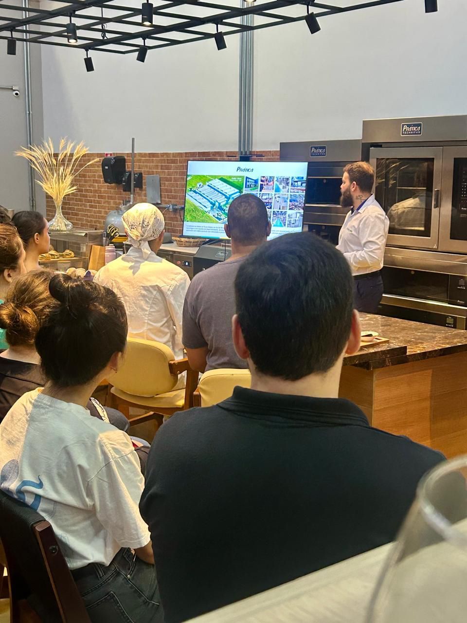 Um homem está fazendo uma apresentação para um grupo de pessoas em uma cozinha.