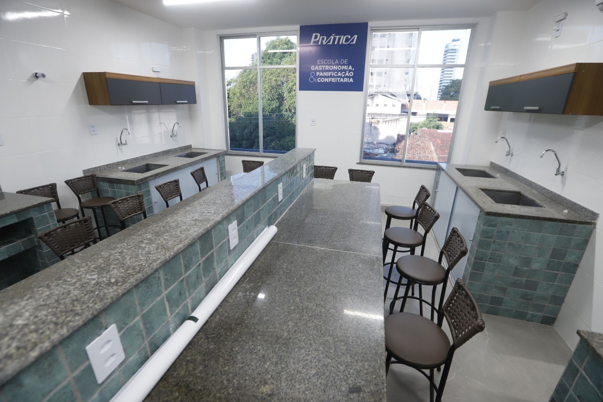 Cozinha com várias pias, balcões e cadeiras. Esquema de cores branco, cinza e marrom.