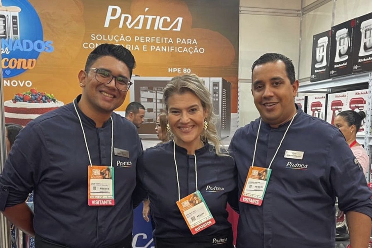 Três pessoas posam para uma foto em frente a uma placa que diz prática