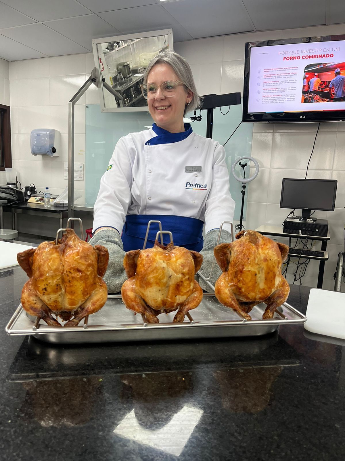 Uma mulher está parada em frente a uma bandeja de frangos assados.