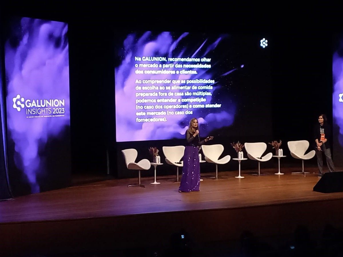 Uma mulher está cantando em um microfone em um palco em frente a uma tela grande.