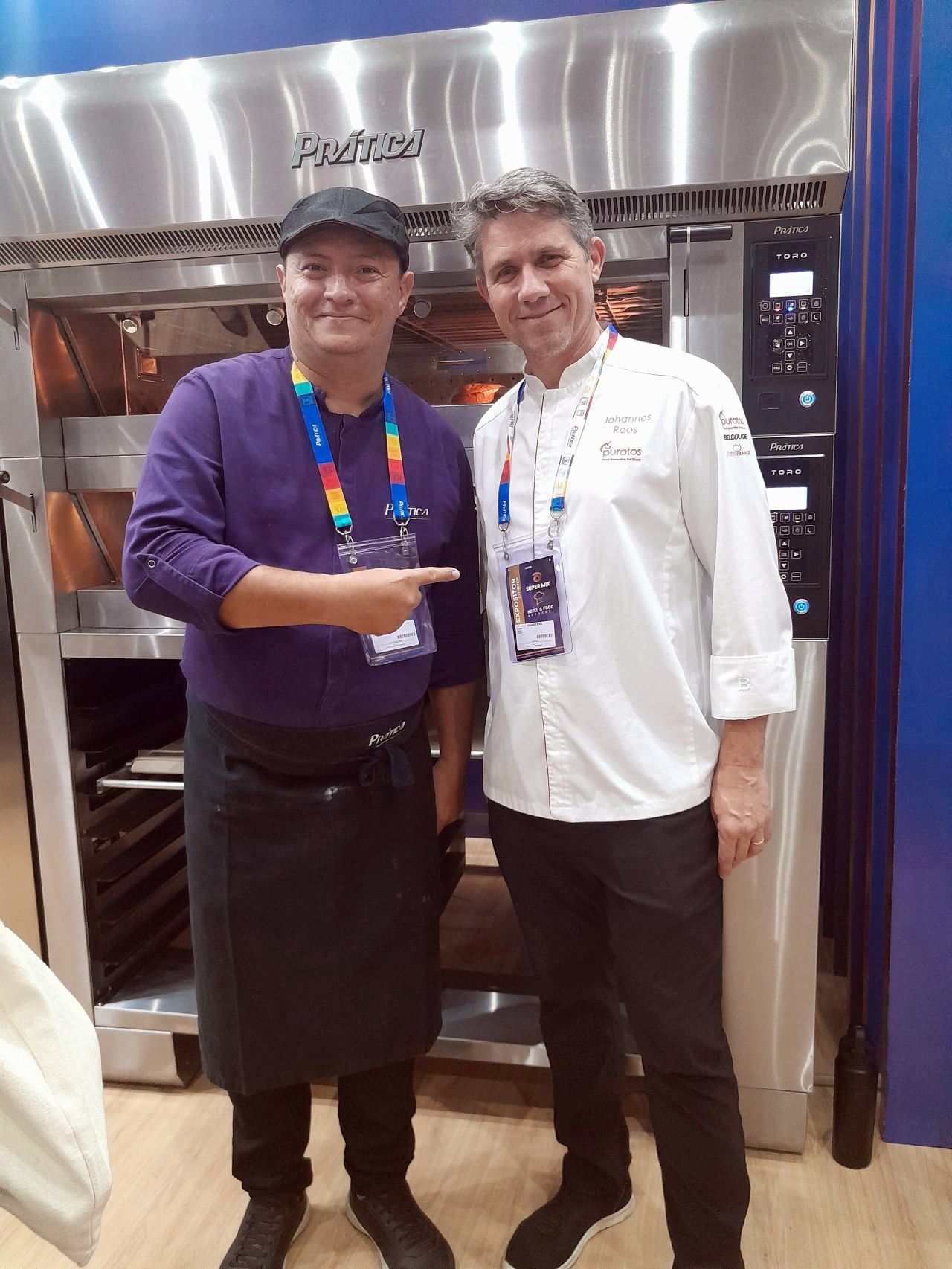 Dois homens posando para uma foto em frente a um forno de aço inoxidável