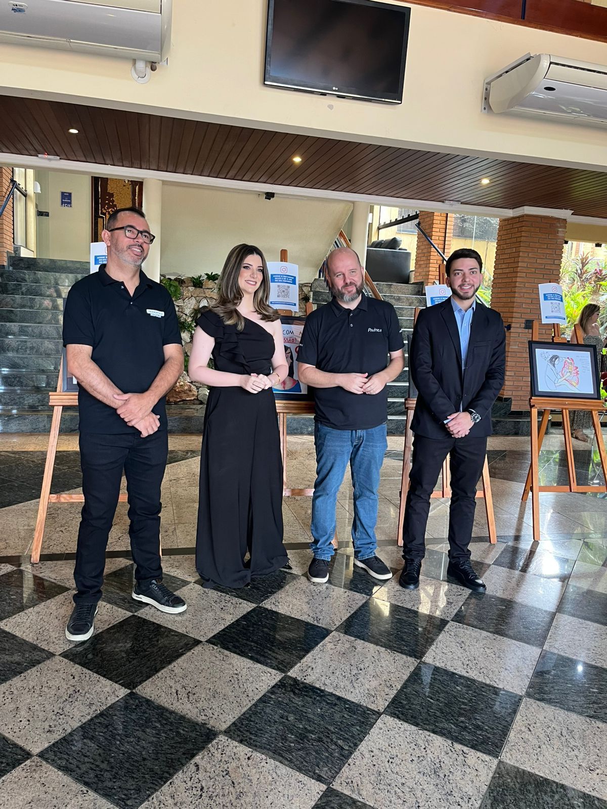 Quatro pessoas em pé perto de cavaletes com arte em uma sala com piso xadrez, um evento formal.