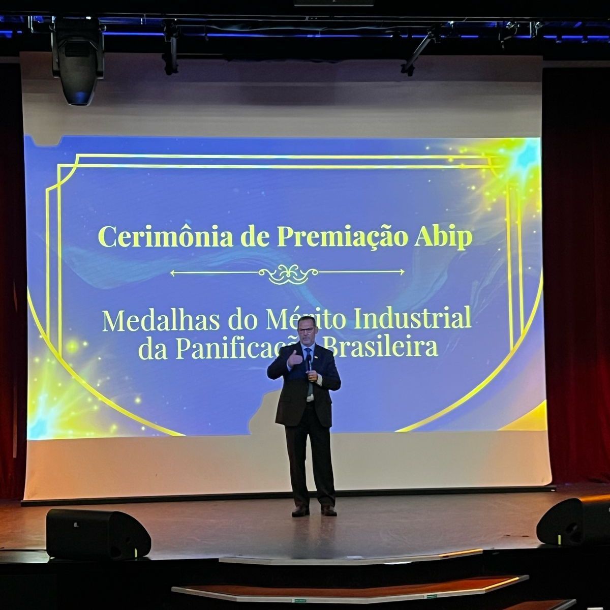 Um homem está em frente a uma tela grande que diz cerimônia de premiação abip