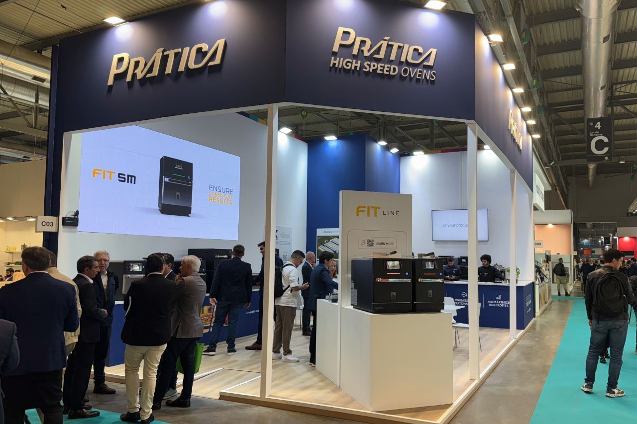 Estande da Pratica em uma feira comercial; marca azul-marinho e dourada, pessoas reunidas ao redor, exibindo produtos.