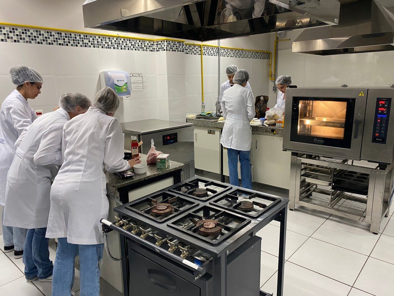 Um grupo de pessoas está em pé ao redor de um fogão em uma cozinha.