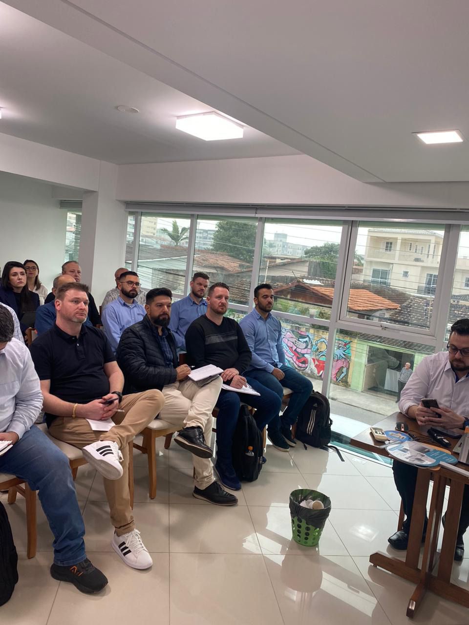 Um grupo de pessoas está sentado em uma sala em frente a uma janela.