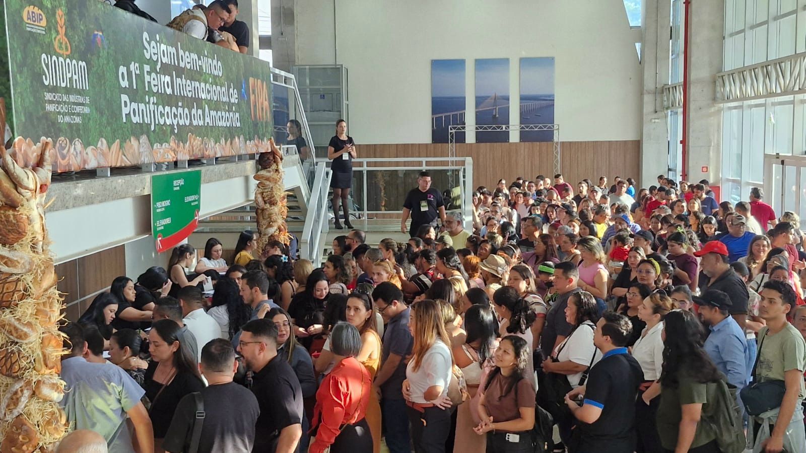 Grande multidão de pessoas em um evento em ambiente fechado. Muitas pessoas estão próximas umas das outras. Uma faixa é visível.