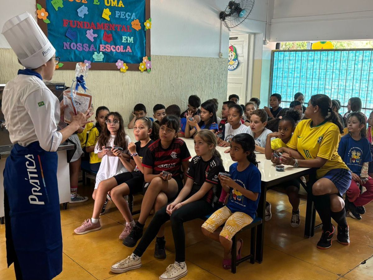 Um chef está em pé na frente de um grupo de crianças sentadas em mesas.