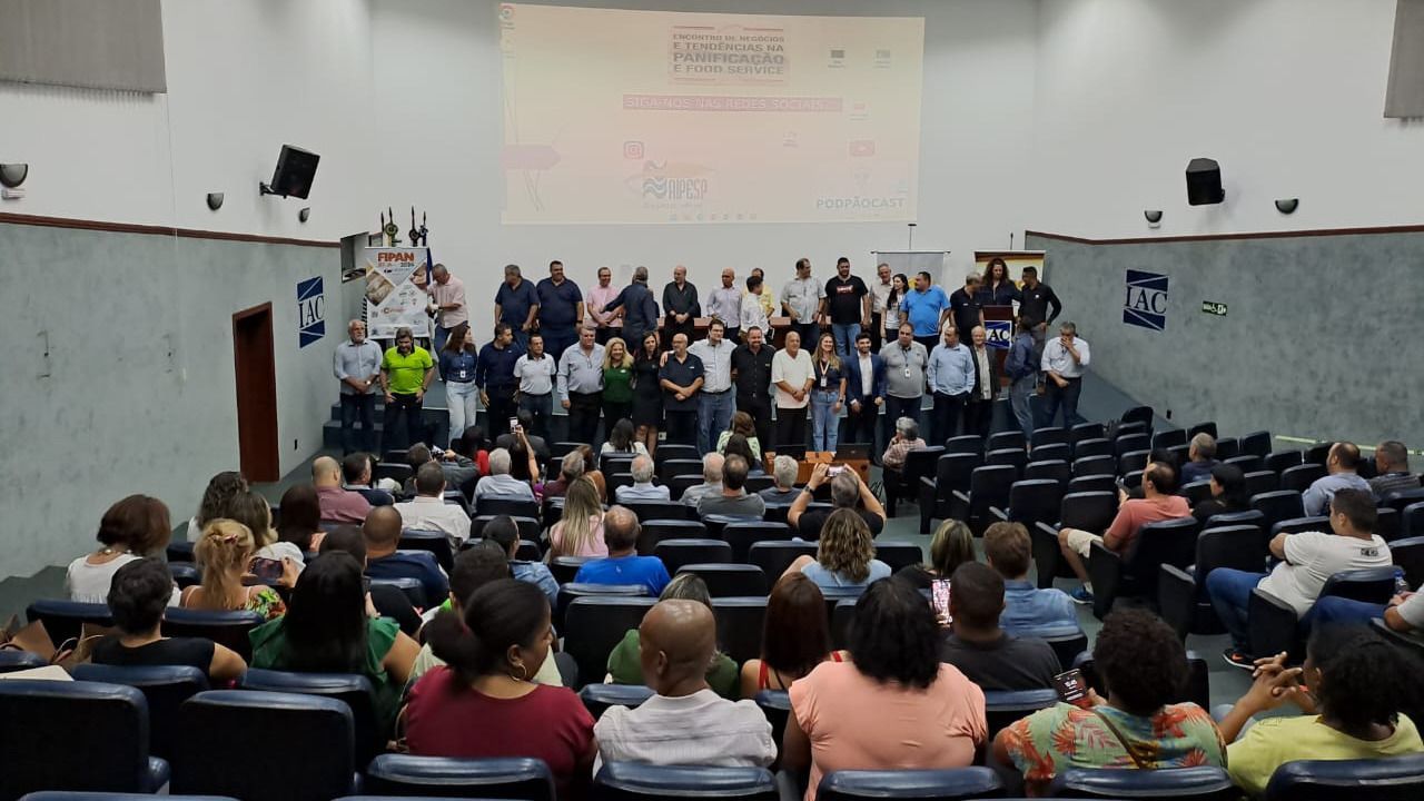 Um grande grupo de pessoas está sentado em um auditório assistindo a uma apresentação.