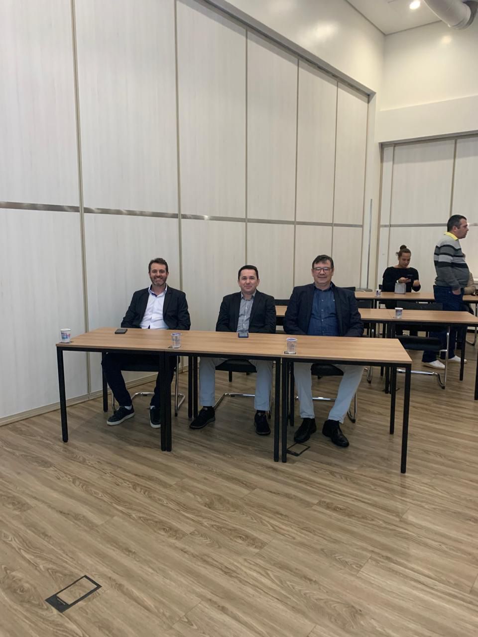 Um grupo de homens está sentado às mesas de uma sala.