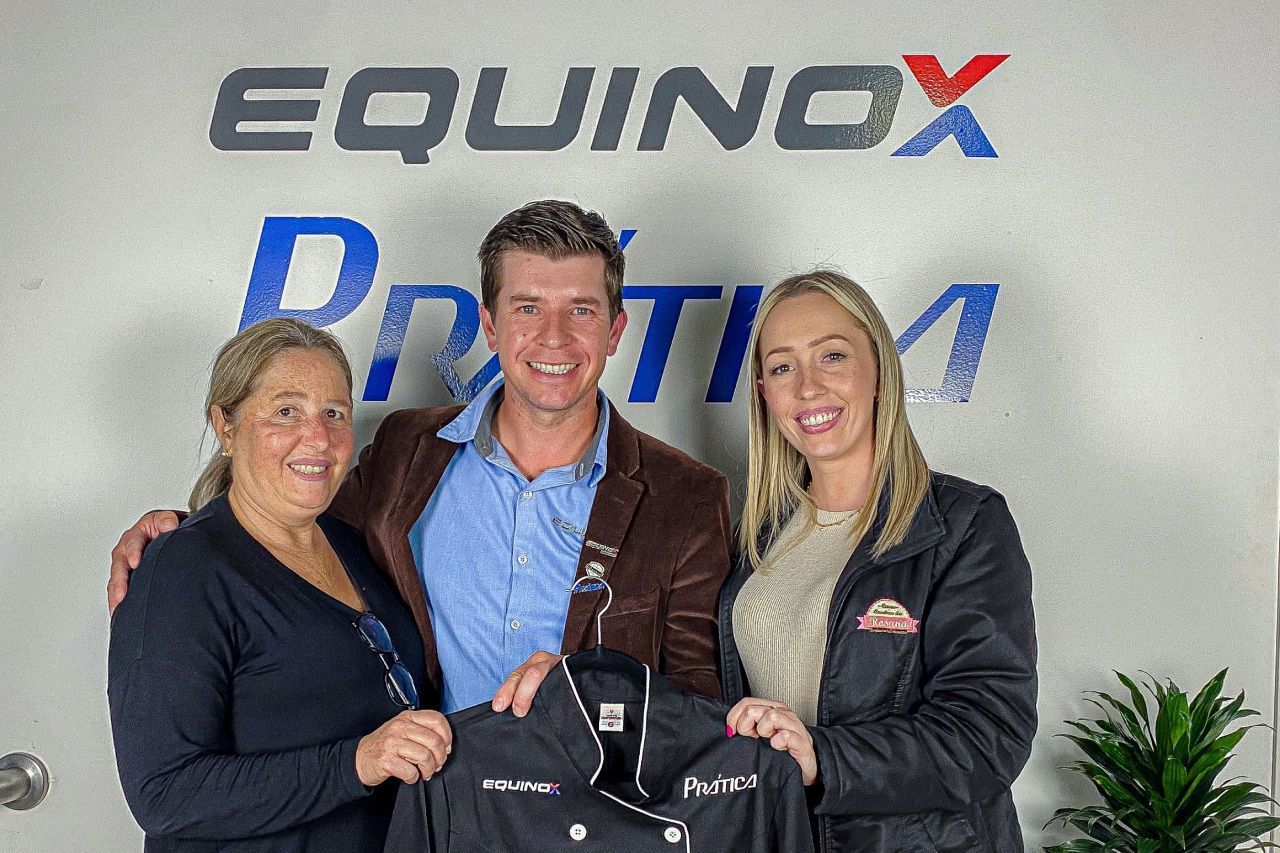 Um homem e duas mulheres estão posando para uma foto em frente a um signo de equinócio.