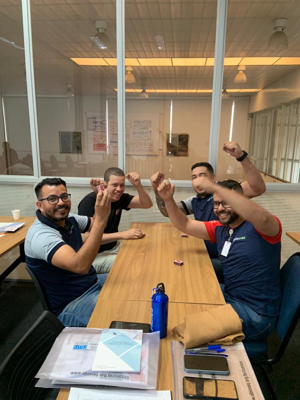 Um grupo de homens está sentado à mesa com os braços no ar.