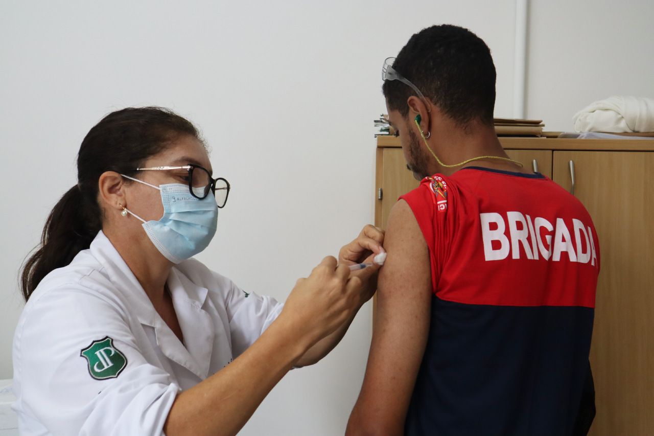 Uma mulher usando uma máscara está dando uma vacina a um homem.