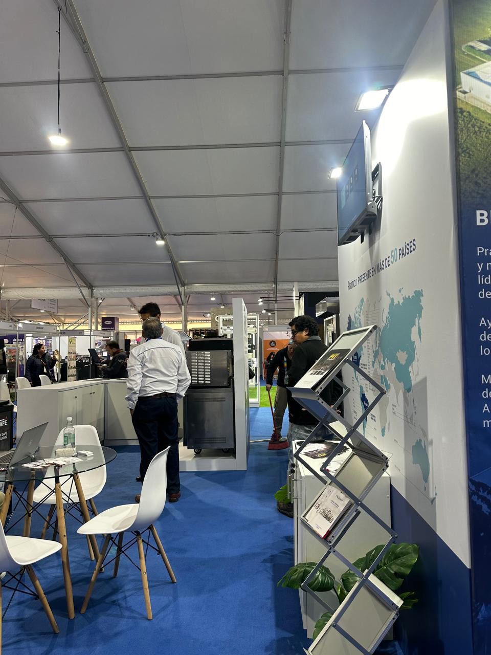 Um grupo de pessoas está de pé em uma sala com mesas e cadeiras.