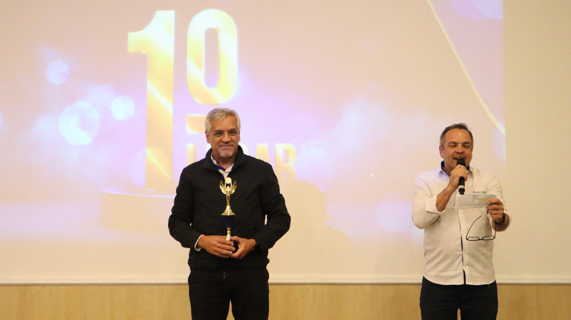 Dois homens estão de pé, um ao lado do outro, em frente a uma tela com o número 10 nela.