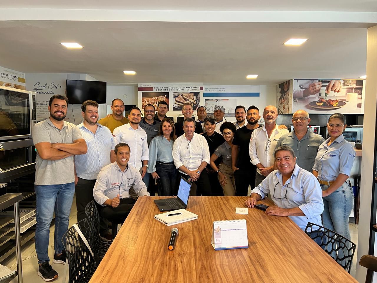 Um grupo de pessoas está de pé ao redor de uma mesa de madeira.