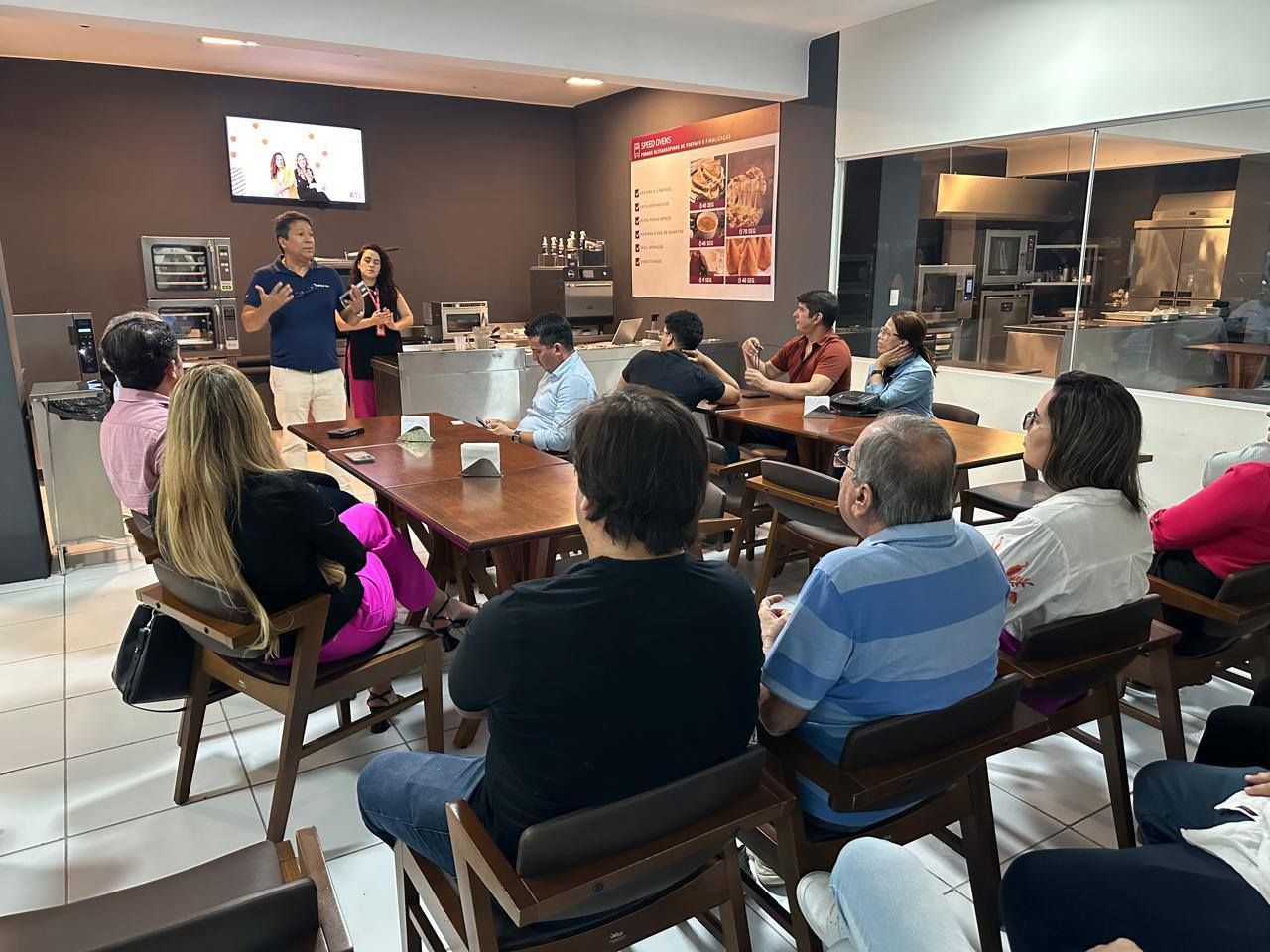 Um grupo de pessoas está sentado em mesas em uma sala.