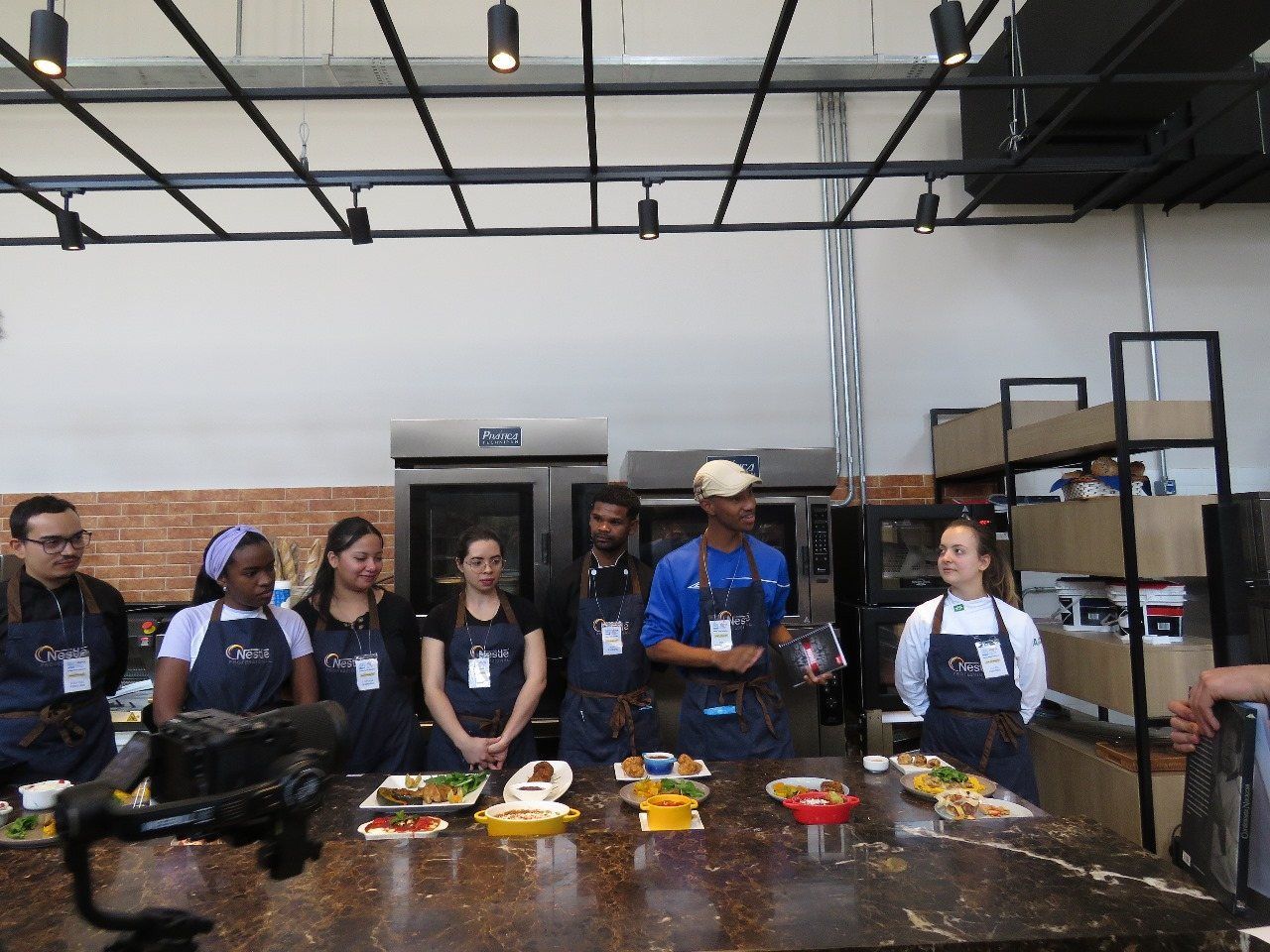 Um grupo de pessoas está em pé ao redor de uma mesa na cozinha.
