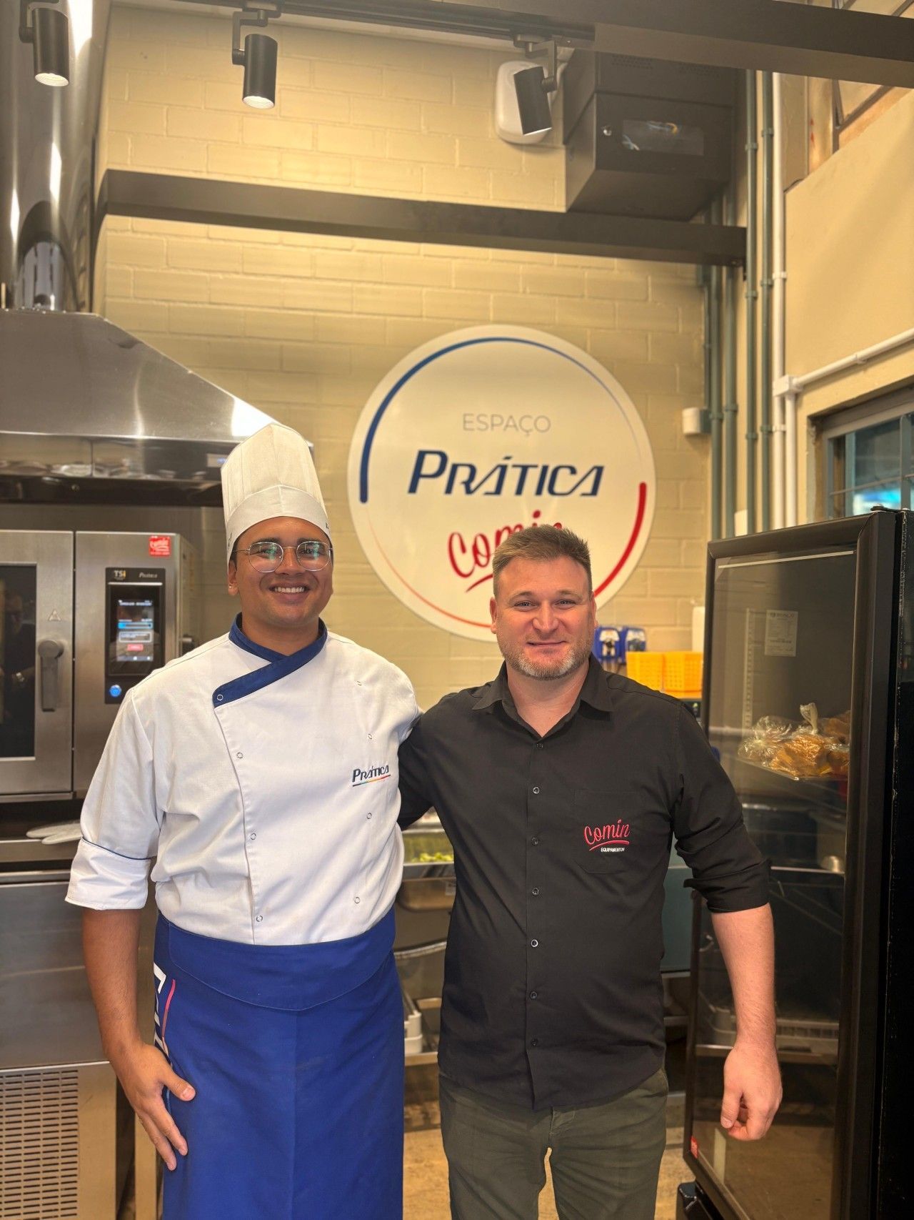 Dois homens estão parados um ao lado do outro em uma cozinha.