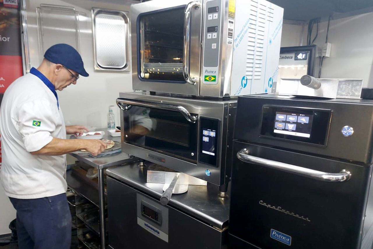 Um homem está parado em frente a uma pilha de fornos em uma cozinha.