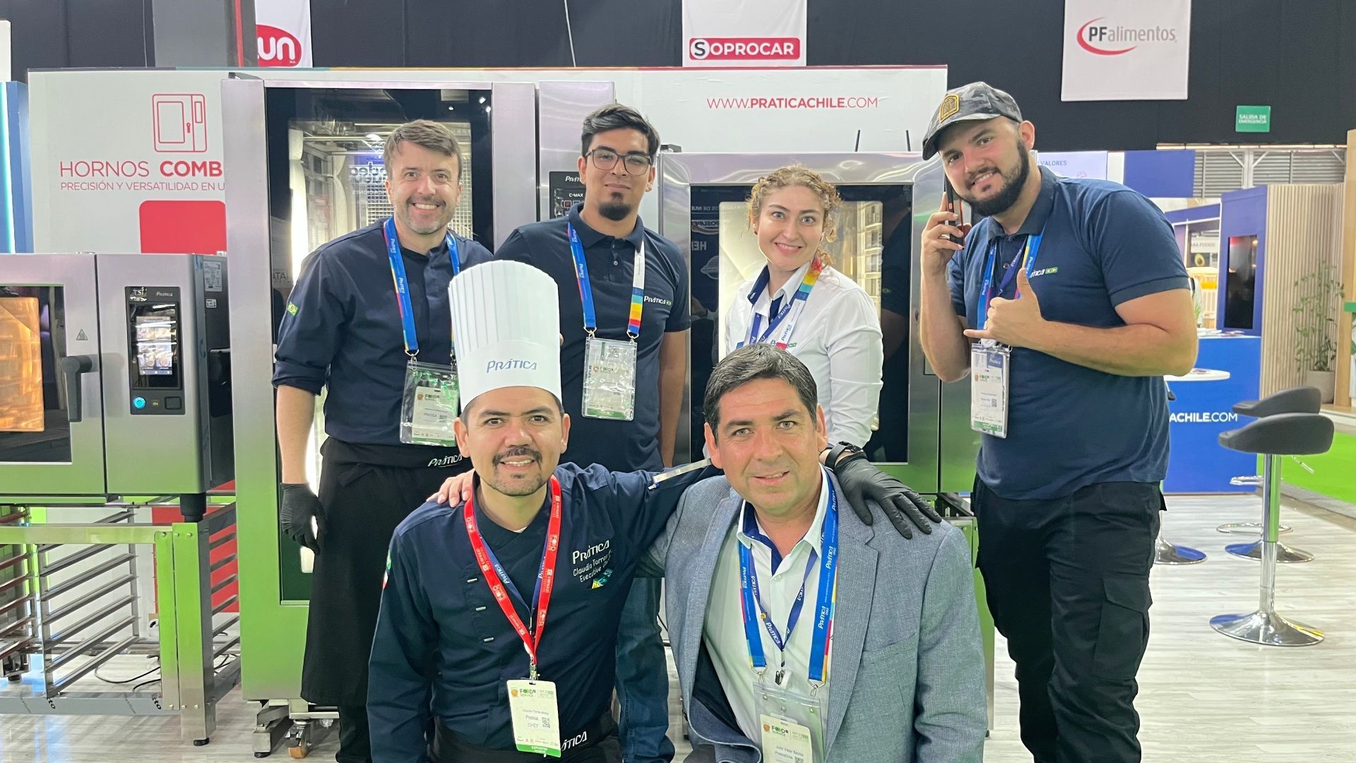 Grupo de seis pessoas sorrindo, posando em frente a fornos comerciais, possivelmente em uma feira comercial.