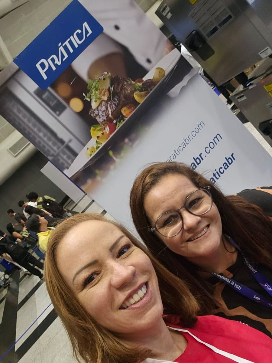 Duas mulheres posando para uma foto em frente a uma placa que diz pratica