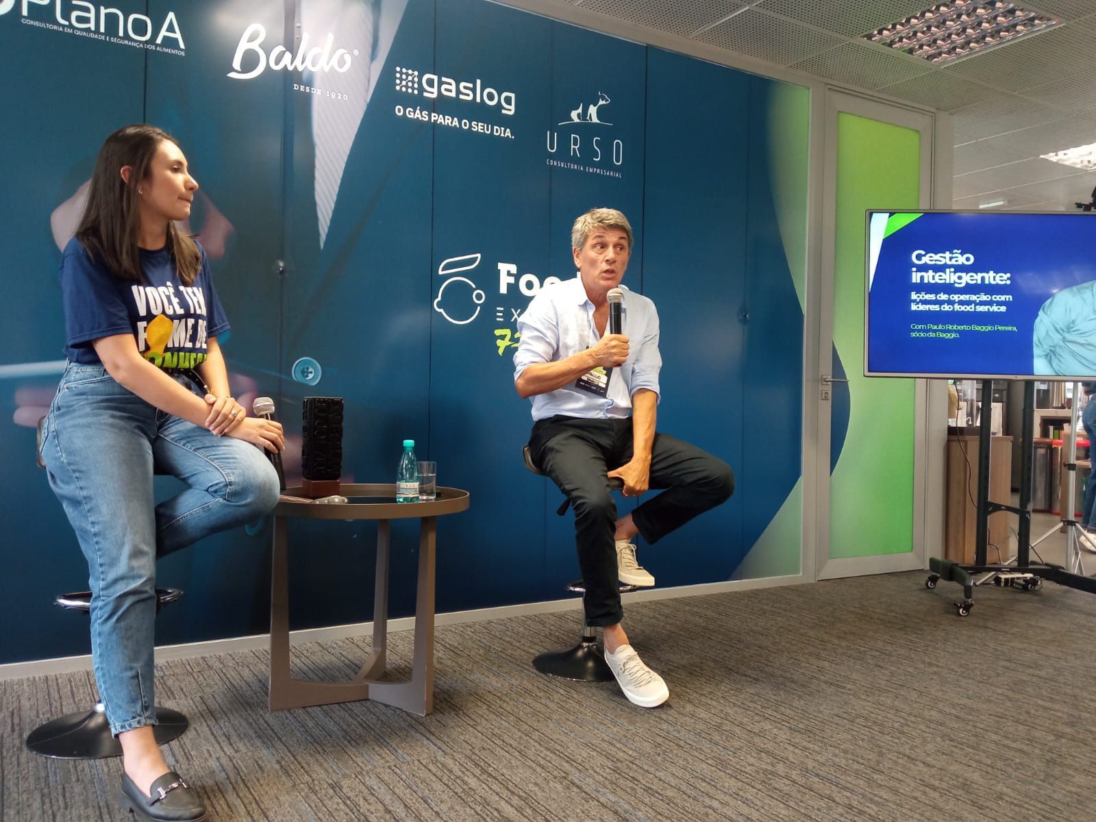 Um homem e uma mulher estão sentados em bancos em frente a uma televisão.